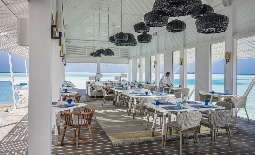 Restaurant Blu Beach Club mit Tischen, blauen Gläsern, weißen Tellern und Blick auf türkisfarbenes Meer