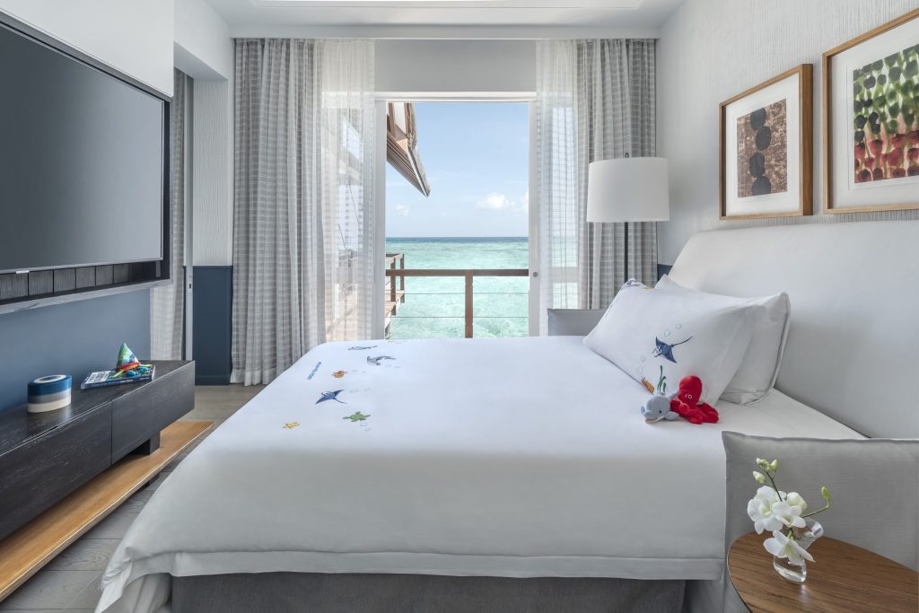 Modernes Hotelzimmer mit Bett, Holztisch, Orchidee, Flachbildfernseher und Meerblick in Landaa Giraavaru