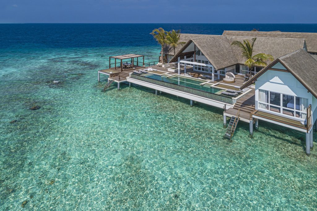 Villa auf Stelzen über türkisfarbenem Wasser mit strohgedecktem Dach und Infinity-Pool auf den