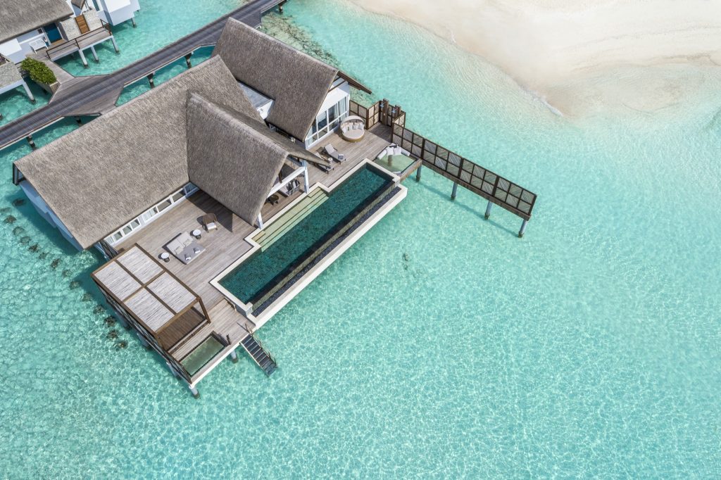 Villa auf Stelzen über türkisblauem Wasser mit Strohdach, Holzterrasse und rechteckigem Infinity-Pool