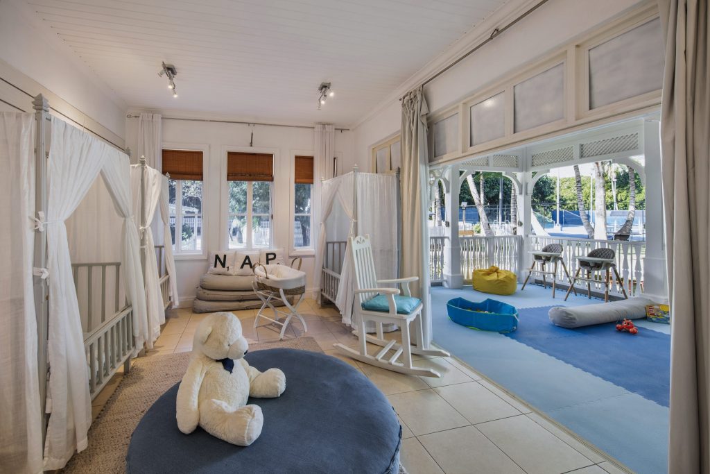 Kinderbereich mit zwei Babybetten, großem weißen Teddybären und Schaukelstuhl auf der Veranda im Heritage Le Telfair