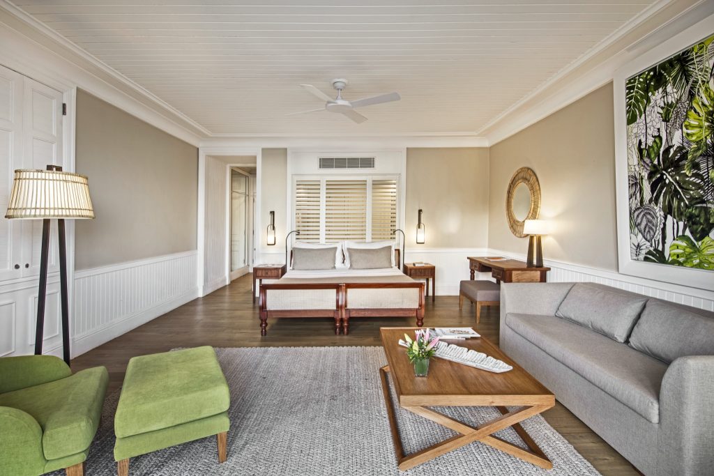 Geräumiges Zimmer der Deluxe Beachfront Suite mit Doppelbett, grünem Sessel, beigen Wänden und Kunstwerk mit Blättern
