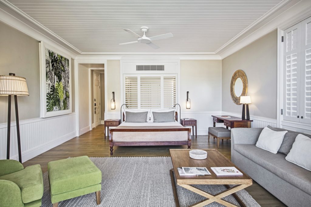 Hell eingerichtetes Zimmer der Deluxe SeaView Suite mit großem Bett, Sofa, grünem Sessel und botanischem Kunstwerk