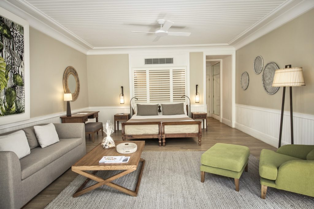 Deluxe Suite Garden Zimmer mit Holzbett, grauer Couch, grünem Sessel und natürlicher Beleuchtung in Heritage Le Telfair.
