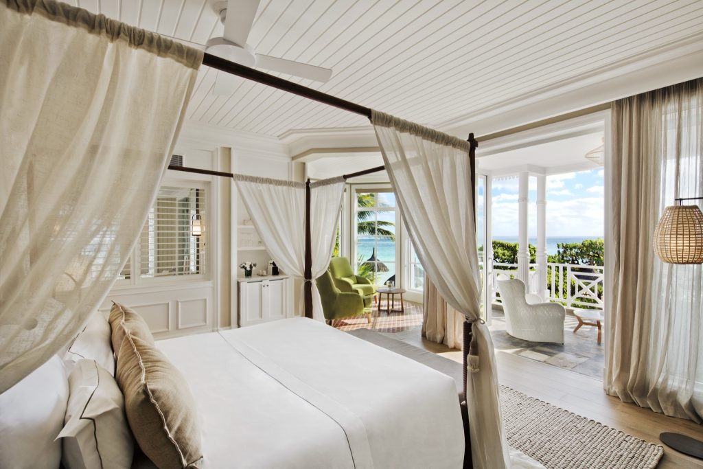 Junior Suite Beach Front Zimmer mit Himmelbett, großen Fenstern, grünem Sessel und Balkon mit Korbsessel