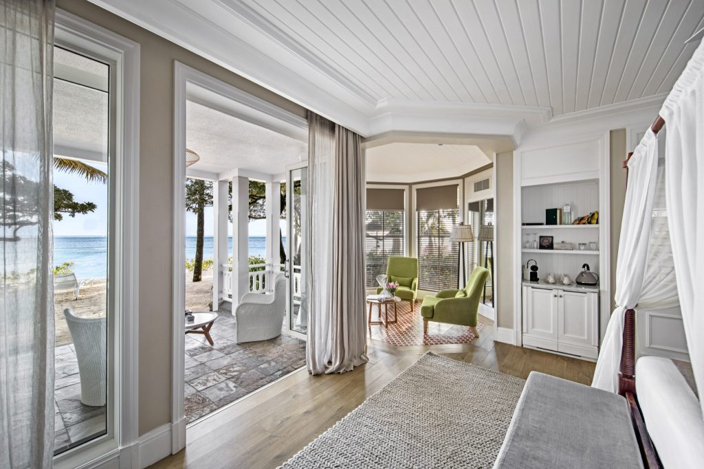 Heller Zimmerbereich der Junior Suite Beach Front mit Holzboden, geflochtenem Teppich, weißer Veranda und Meerblick