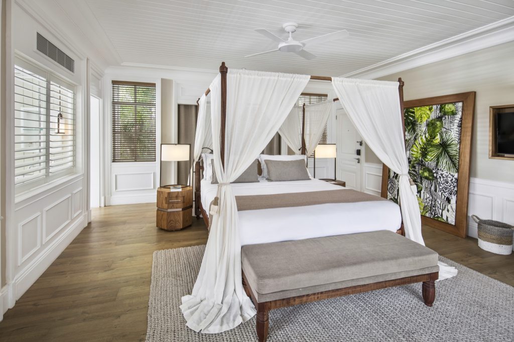 Junior Suite Garden View mit weißem Himmelbett, Holzboden, rundem Holztisch und Pflanzenbild an der Wand