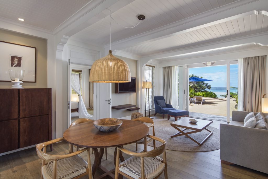 Wohn- und Essbereich der Ocean Suite im Heritage Le Telfair mit Holz- und Rattanmöbeln, Glasschiebetüren und Strandblick