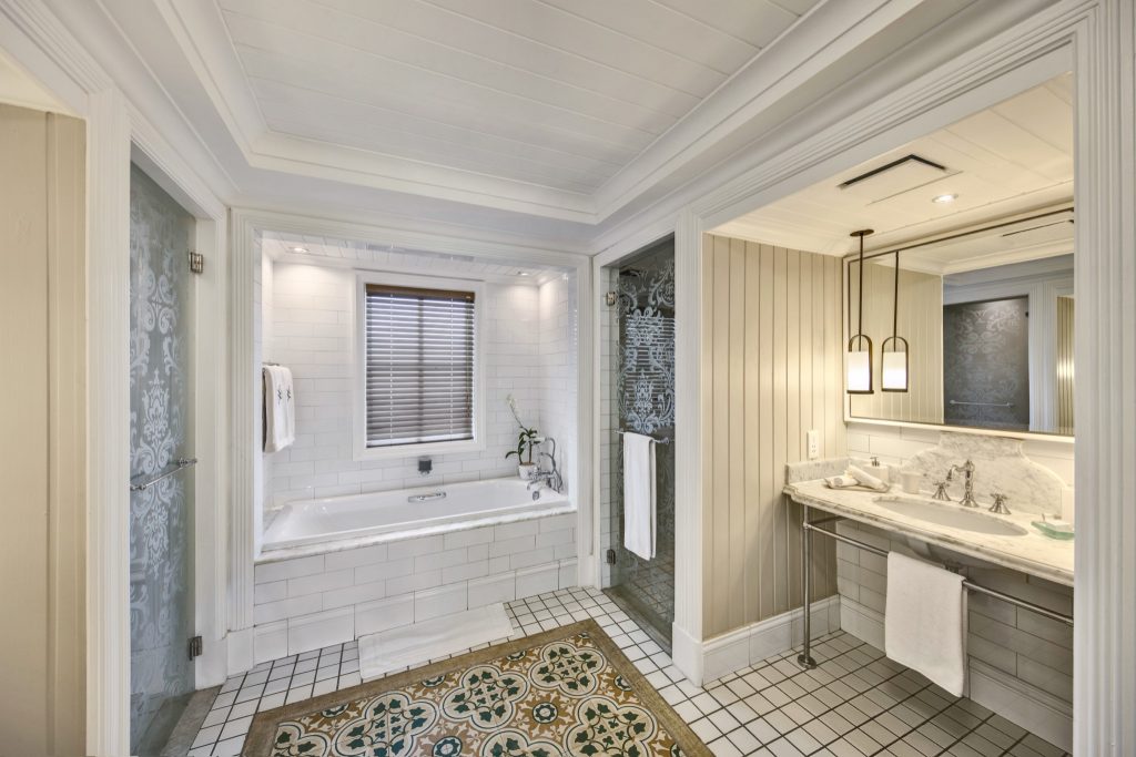Badezimmer mit freistehender weißer Badewanne, Duschecke mit Glastür, Marmorwaschbecken und cremefarbenen Fliesen.