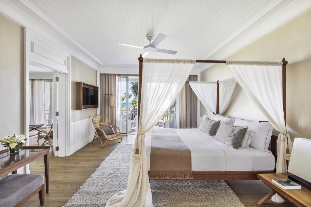 Senior Suite Sea View Zimmer mit Himmelbett, Holzboden, Rattan-Stuhl und Balkon mit Palmenblick in Mauritius