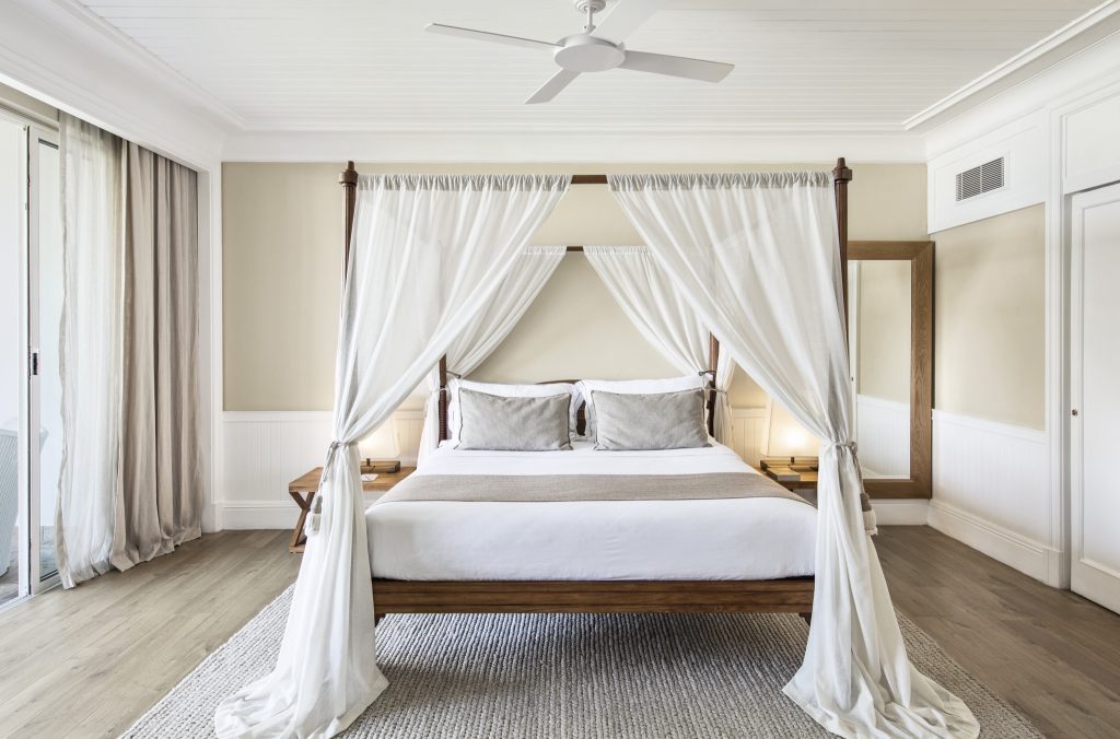 Schlafzimmer der Senior Suite mit Himmelbett, weißen Vorhängen und Holzrahmen im Heritage Le Telfair