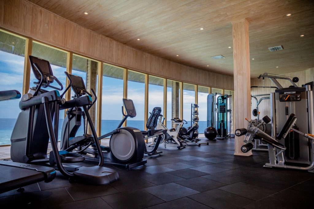 Moderner Fitnessraum mit Panoramafenstern, Laufbändern, Crosstrainern und Kraftmaschinen mit Blick aufs Meer