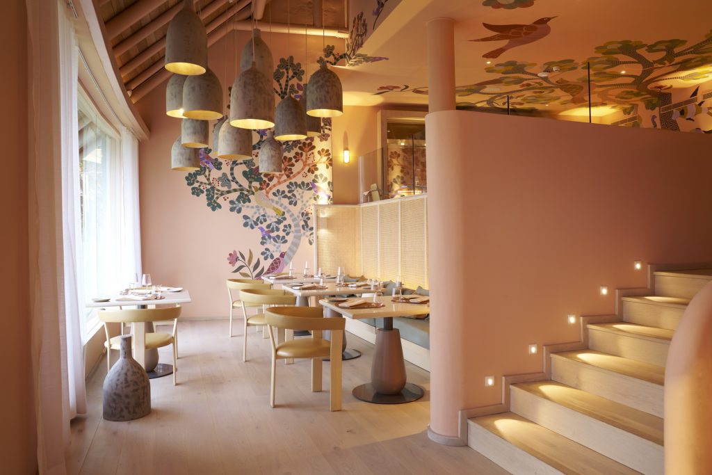 Essbereich im Restaurant Amari mit runden Tischen, hellbraunen Stühlen, Holzboden und blumigen Wandmalereien