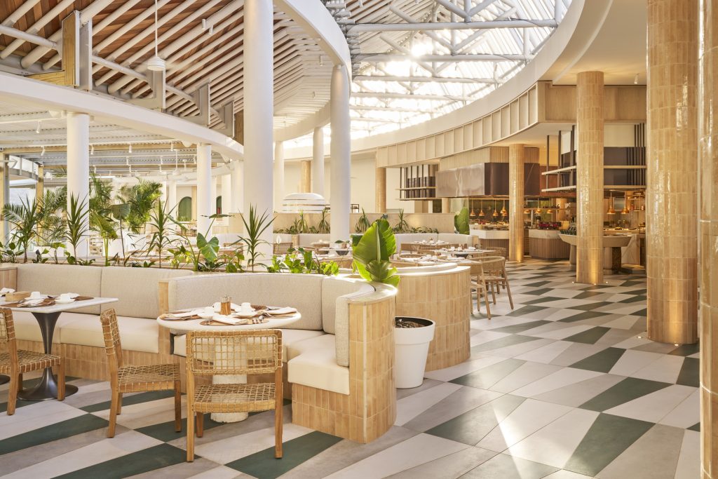 Helles Restaurant Mondo mit kreisförmigen Sitzbereichen, Holztischen, geflochtenen Stühlen und großen Glasdach in Lux Belle.
