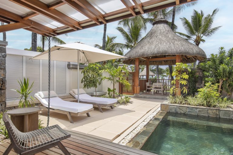 Außenbereich des Lux Belle Mare mit Pool, zwei weißen Liegestühlen unter Sonnenschirm und Strohdach-Pavillon