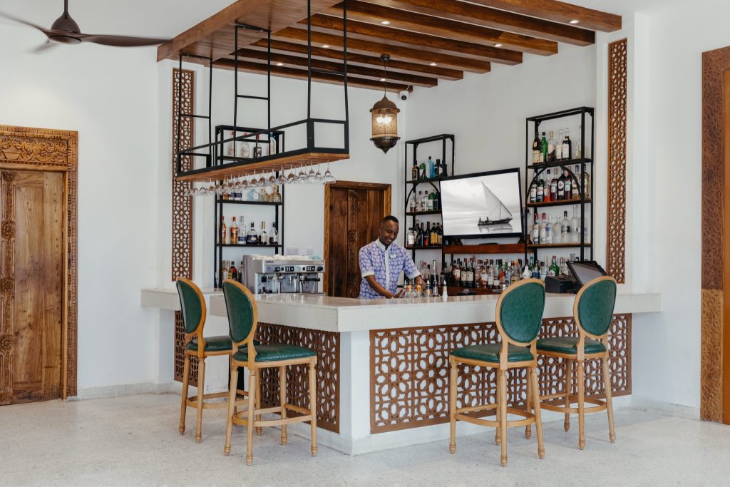 Hotelbar Lux Marijani mit Holztheke, vier grünen Barstühlen, Spirituosenregal und Flachbildfernseher mit Segelboot