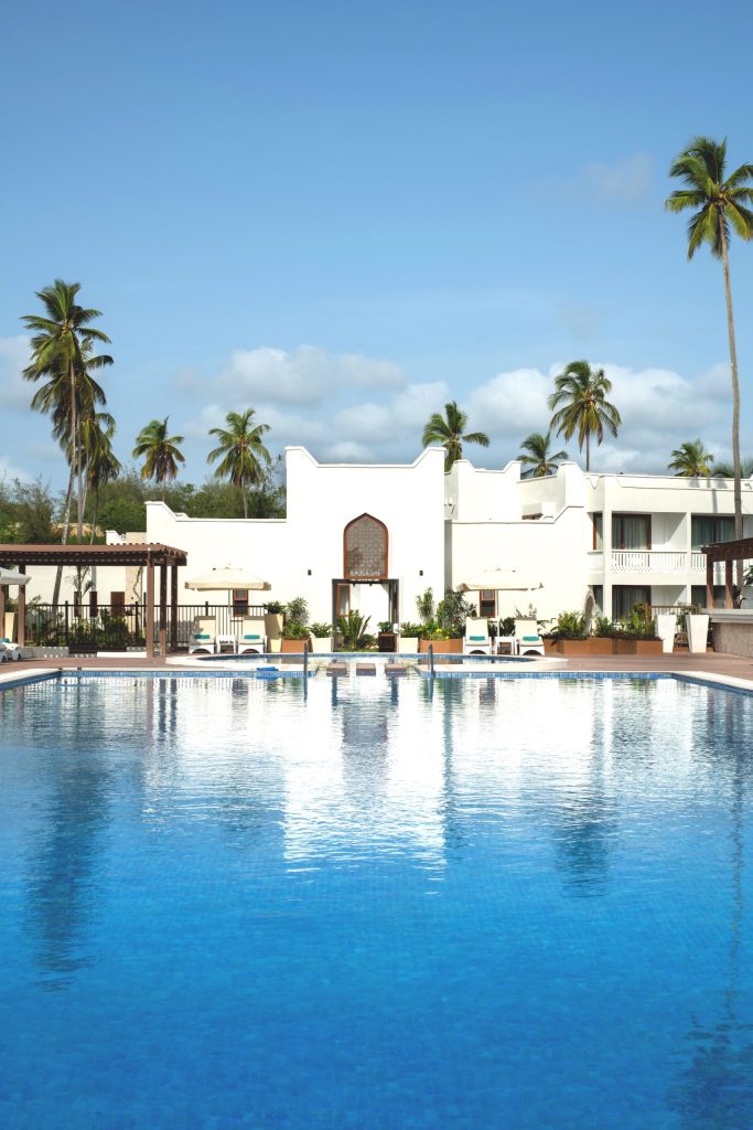 Hotelpool bei Lux Marijani mit weißen Sonnenschirmen, Liegestühlen und Palmen unter blauem Himmel in Sansibar