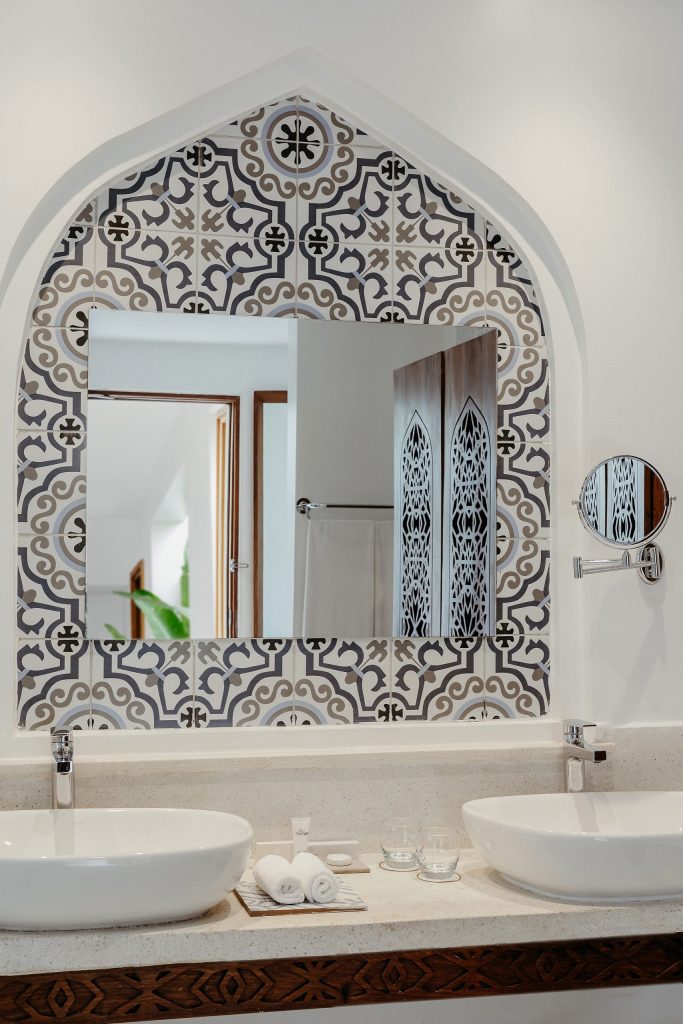 Badezimmer mit zwei Waschbecken, großem Spiegel in geometrisch gemusterter Wand, Handtüchern und Glasbechern