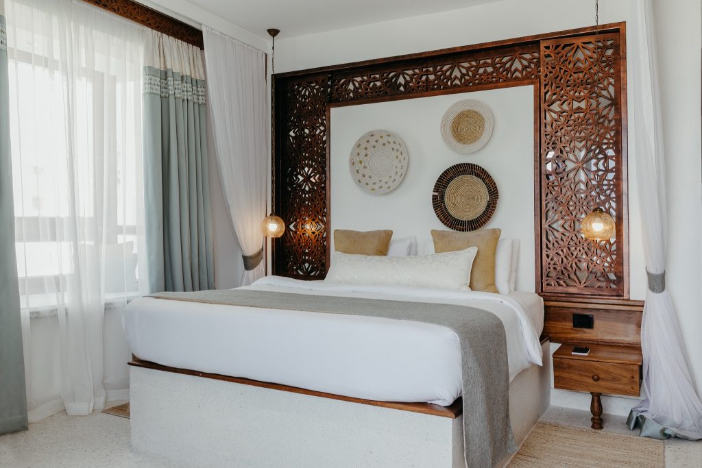Hotelzimmer im Lux Marijani mit großem Bett, geschnitztem Holzkopfteil, weißen und beigen Bettwäschen.