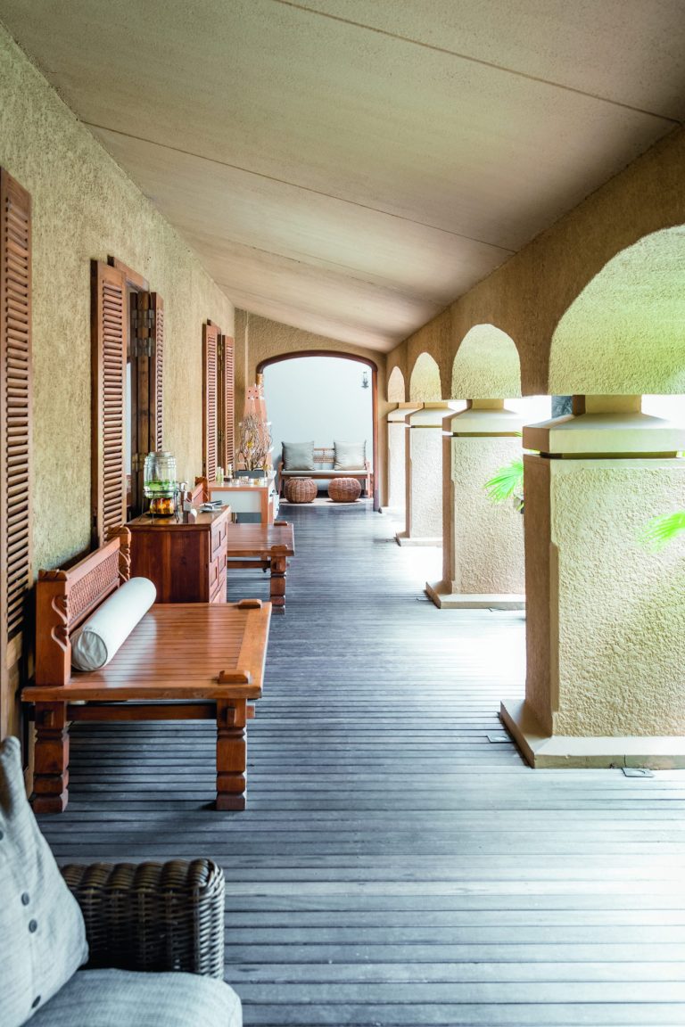 Überdachter Hotelgang mit Holzfensterläden, Holzmöbeln und Rundbögen im Mauricia Beachcomber Resort & Spa