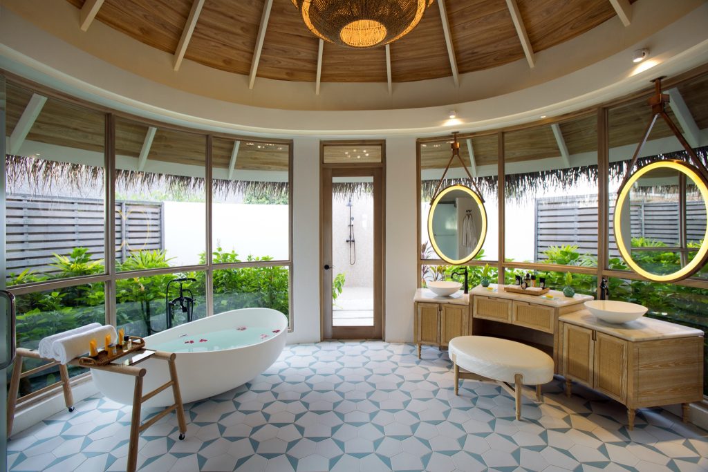 Badezimmer mit freistehender Badewanne vor großen halbkreisförmigen Fenstern und Holzdecke im Milaidhoo Island
