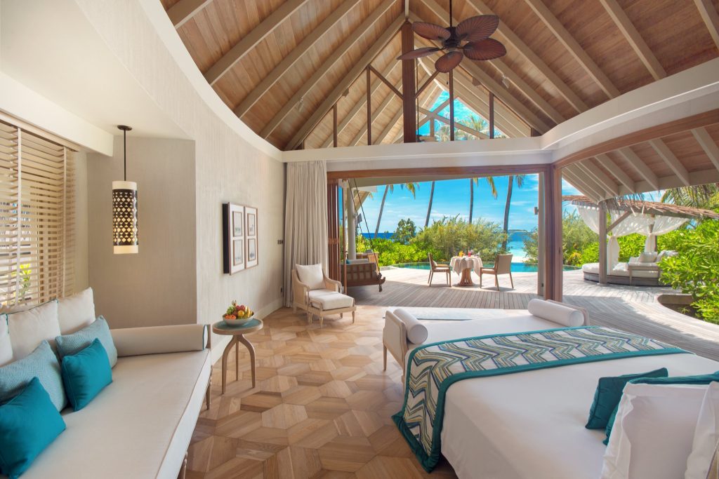 Zimmer der Milaidhoo Island Beach Pool Villa mit großem Bett, Teetisch, Holzfußboden und Blick auf Terrasse und Ozean