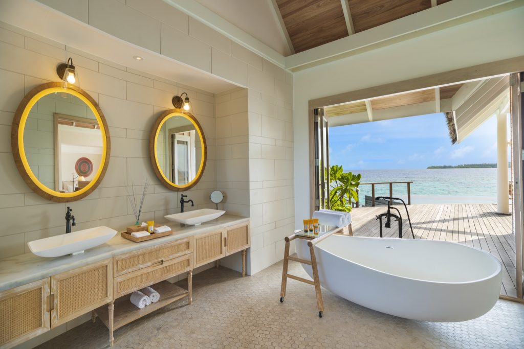 Badezimmer mit freistehender Badewanne, zwei runden Spiegeln und Glasfront mit Blick auf das Meer
