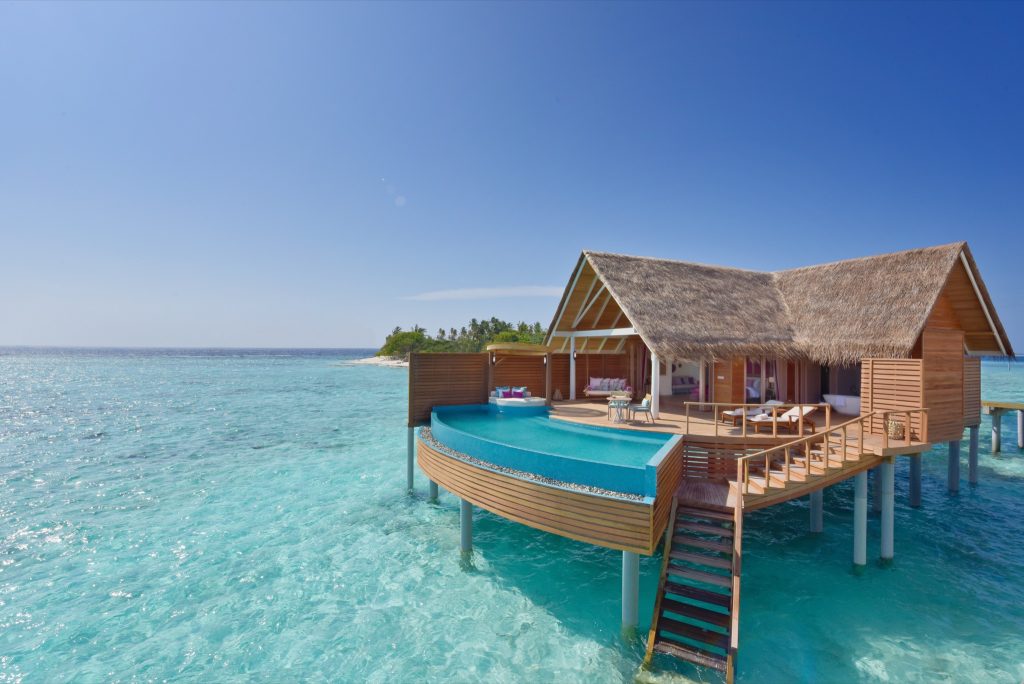Überwasserbungalow aus Holz mit Strohdach und Infinity-Pool über türkisblauem Wasser auf den