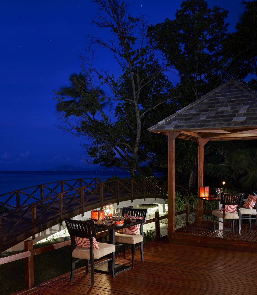Terrasse des Restaurants Sakura im NIVA Labriz Seychelles bei Nacht mit Holztischen, roten Kissen und Meerblick