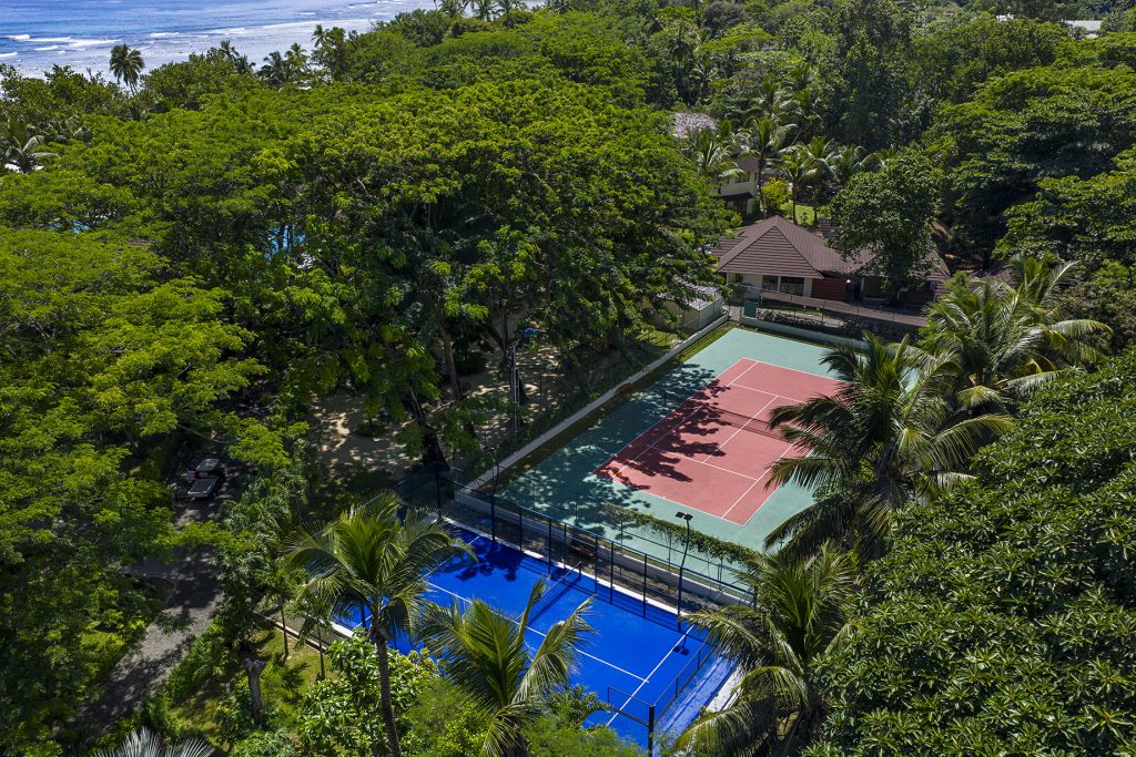 Tennisplatz und blaues Padel-Spielfeld umgeben von grüner Vegetation mit Meer im Hintergrund bei NIVA Labriz Seychelles