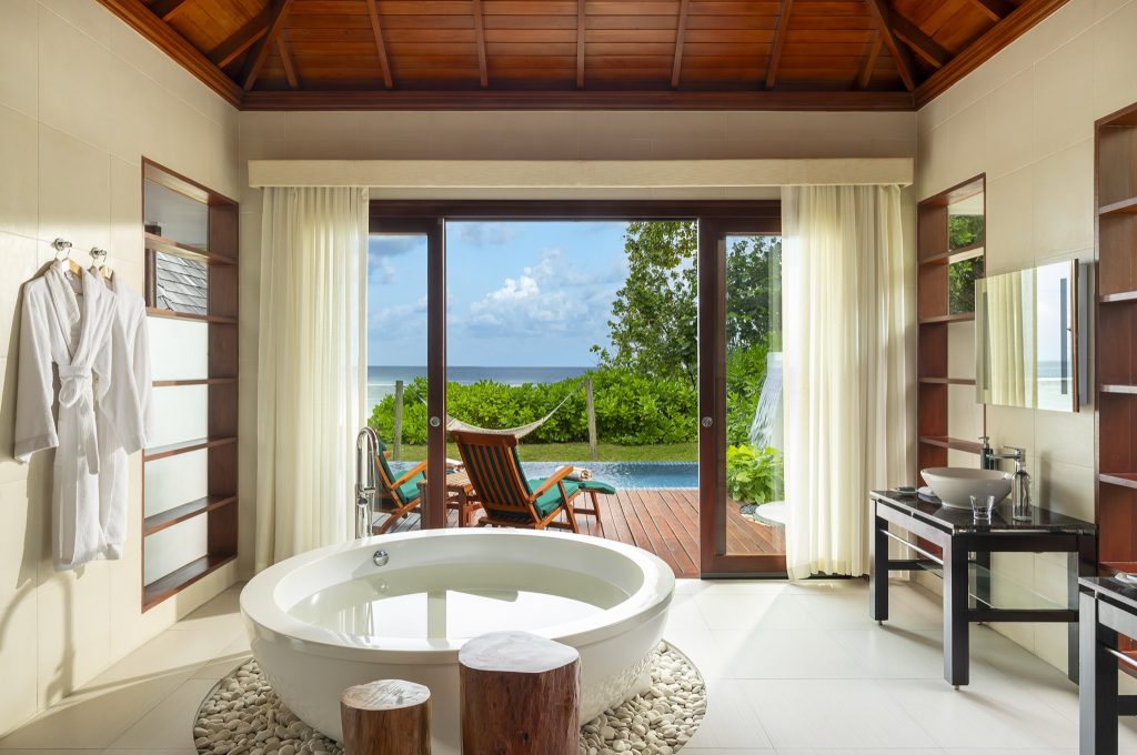 Badezimmer der Beach Sanctuary Pool Villa mit freistehender Badewanne, großen Fenstern und Blick auf Terrasse und Pool