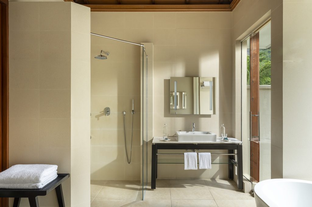 Modernes Badezimmer der Beach Villa im NIVA Labriz Seychelles mit Glasdusche, rechteckigem Spiegel und beigefarbenen Fliesen