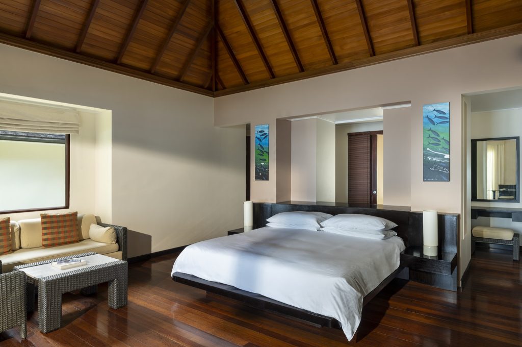 Hotelzimmer der Beach Villa mit großem Bett, Rattan-Sesseln, Holzboden und spitz zulaufender Holzdecke