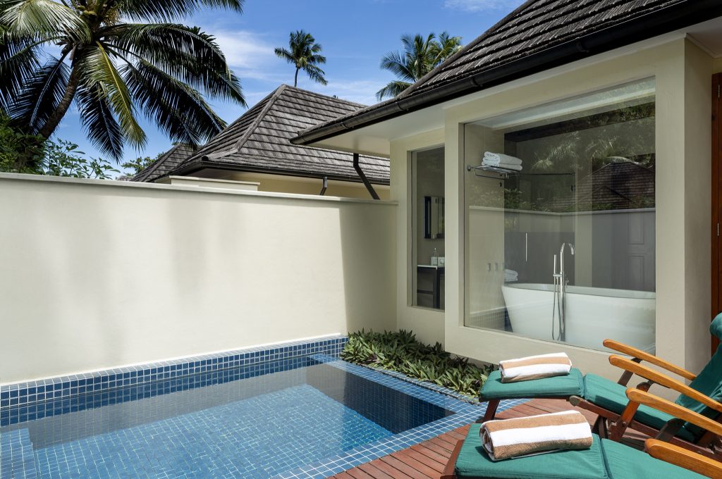 Privater Außenbereich mit blau gefliestem Pool, weißen Mauern, zwei grünen Liegestühlen und freistehender Badewanne hinter.