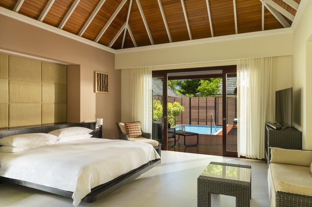 Hotelzimmer mit großem Bett, Rattan-Sitzgruppe und Poolblick durch große Glastür in der Garden Oasis Pool Villa