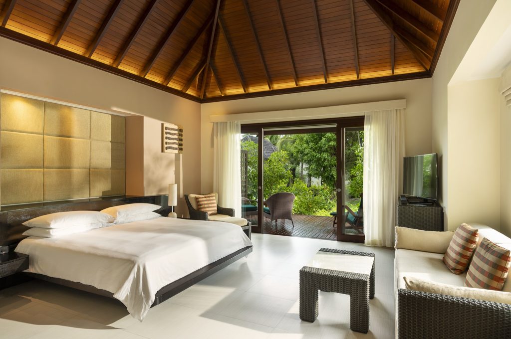 Modernes Garden Villa Zimmer mit großem Bett, Sofa, Flachbildfernseher und Holzterrasse mit Pflanzen auf den
