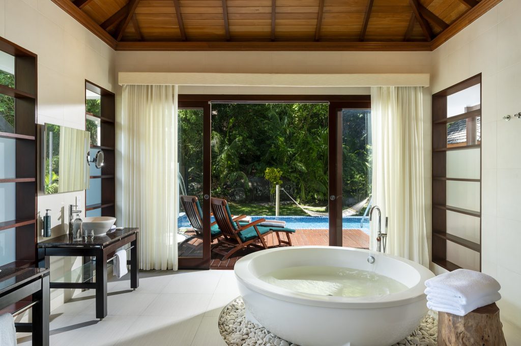 Badezimmer mit runder freistehender Badewanne, weißen Kieselsteinen, zwei Waschbecken und Glastüren zur Terrasse