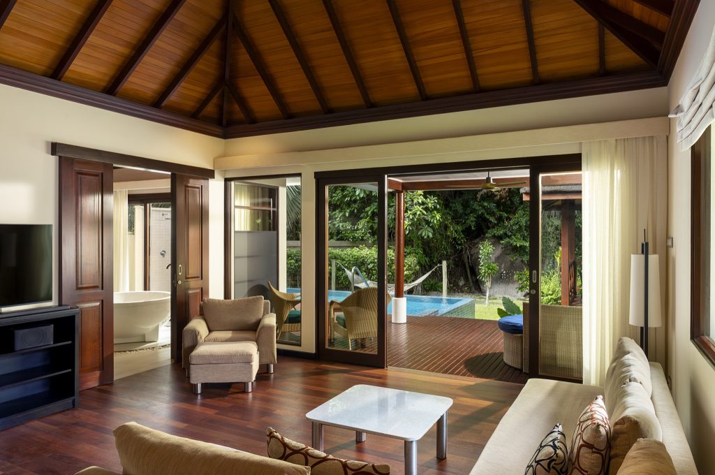 Jungle Sanctuary Pool Villa Sitzbereich mit beigen Polstermöbeln, dunklem Holzboden und Terrasse mit Pool auf den