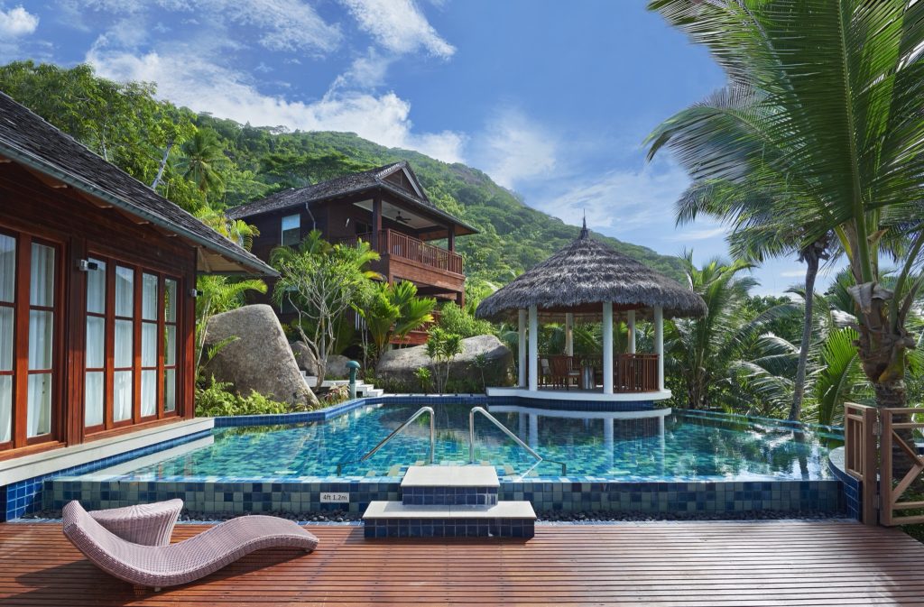 Hotelpool mit blauen Mosaikfliesen, hölzerner Terrasse, Strohpavillon und Palmen auf den