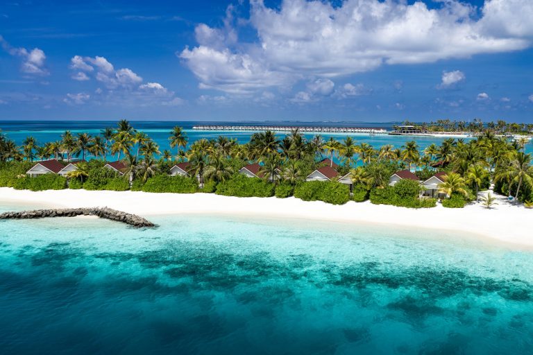 Reihe von Bungalows mit roten Dächern und Poolvillen umgeben von Palmen an weißem Strand