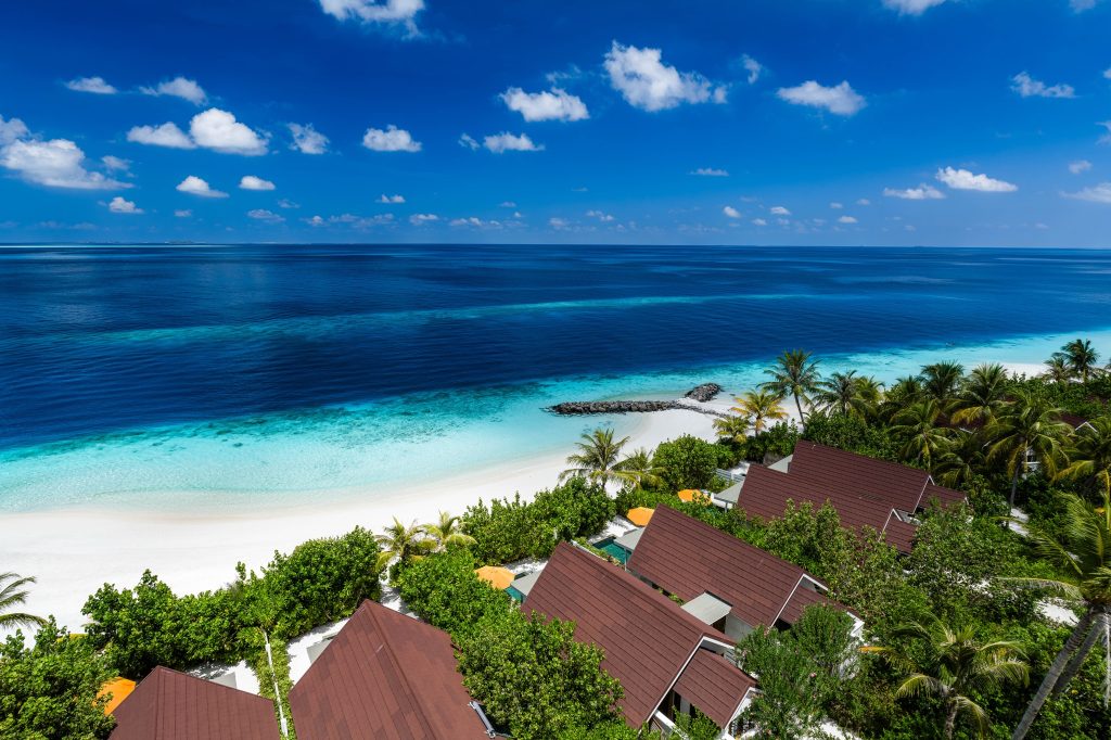 Vogelperspektive auf OBLU SELECT Lobigili Sunnest Beach Pool Villa mit Palmen, Sandstrand und türkisfarbenem Meer