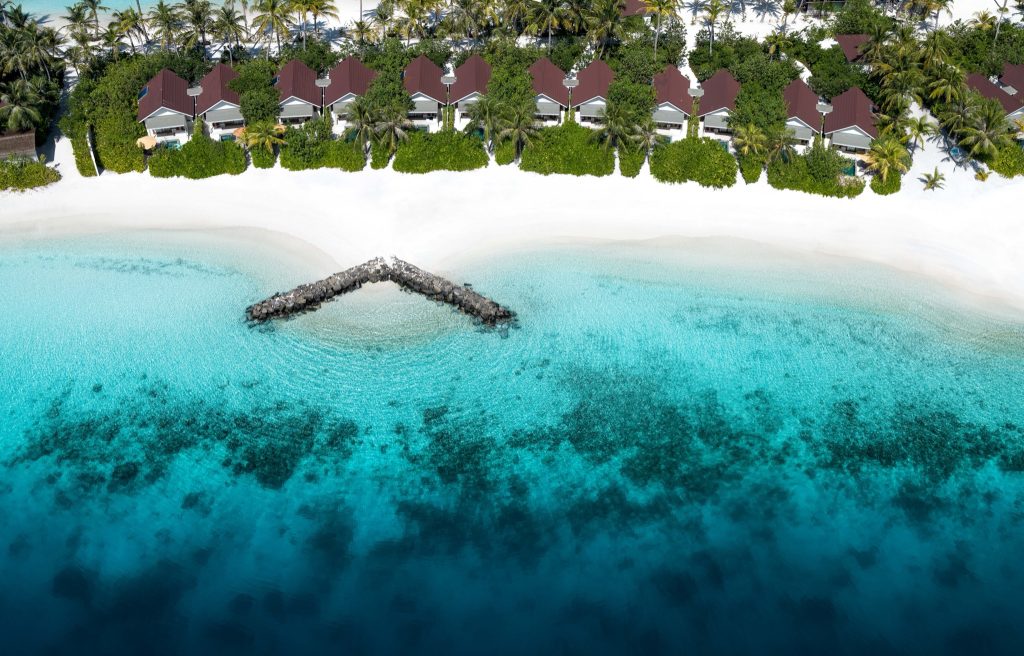 Luftaufnahme der Sunnest Beach Pool Villas mit braunen Dächern an weißem Sandstrand und türkisfarbenem Wasser