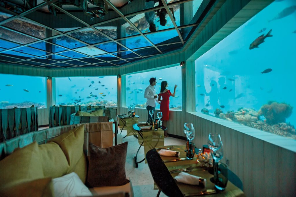 Unterwasserrestaurant M6M mit großen Glasfenstern und Blick auf die Meereswelt, Tische mit gedecktem Geschirr.