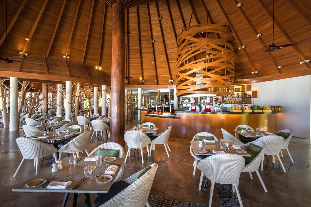 Restaurant The Palms mit hölzerner Decke, weißen geflochtenen Stühlen und Tresen aus Holz im Ozen Life Maadhoo