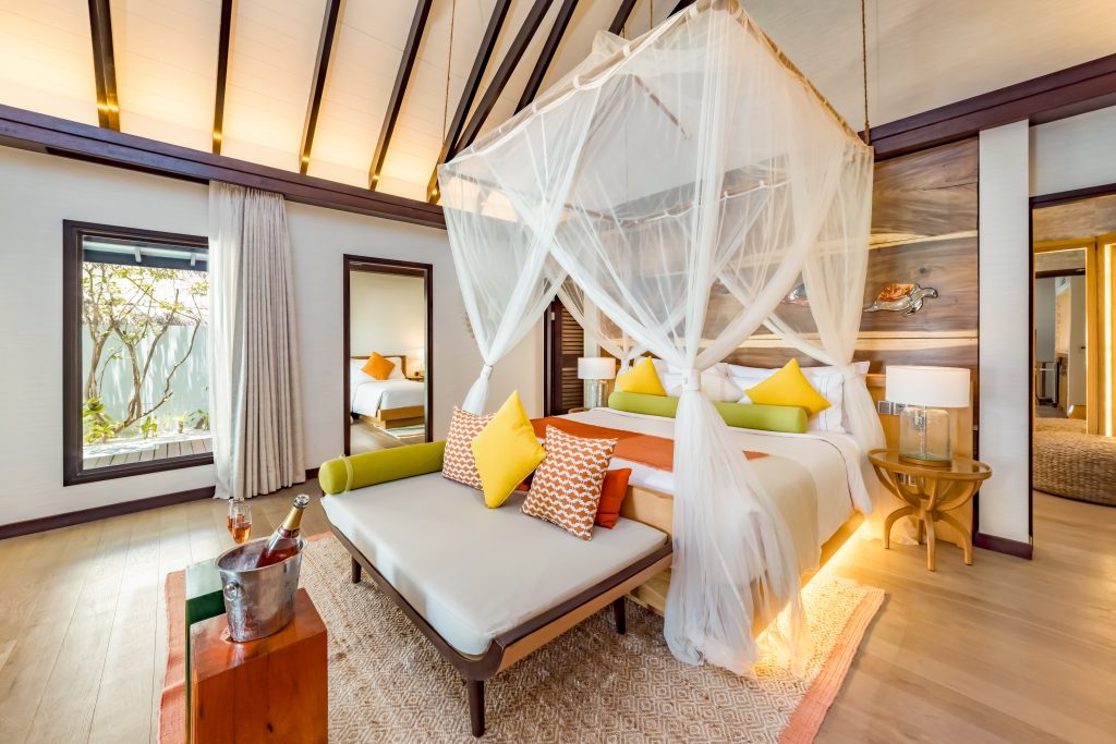 Hotelzimmer Earth Pool Pavilion mit Himmelbett, Holzmöbeln, großen Fenstern und Pflanzen am Fenster im Ozen Life Maadhoo