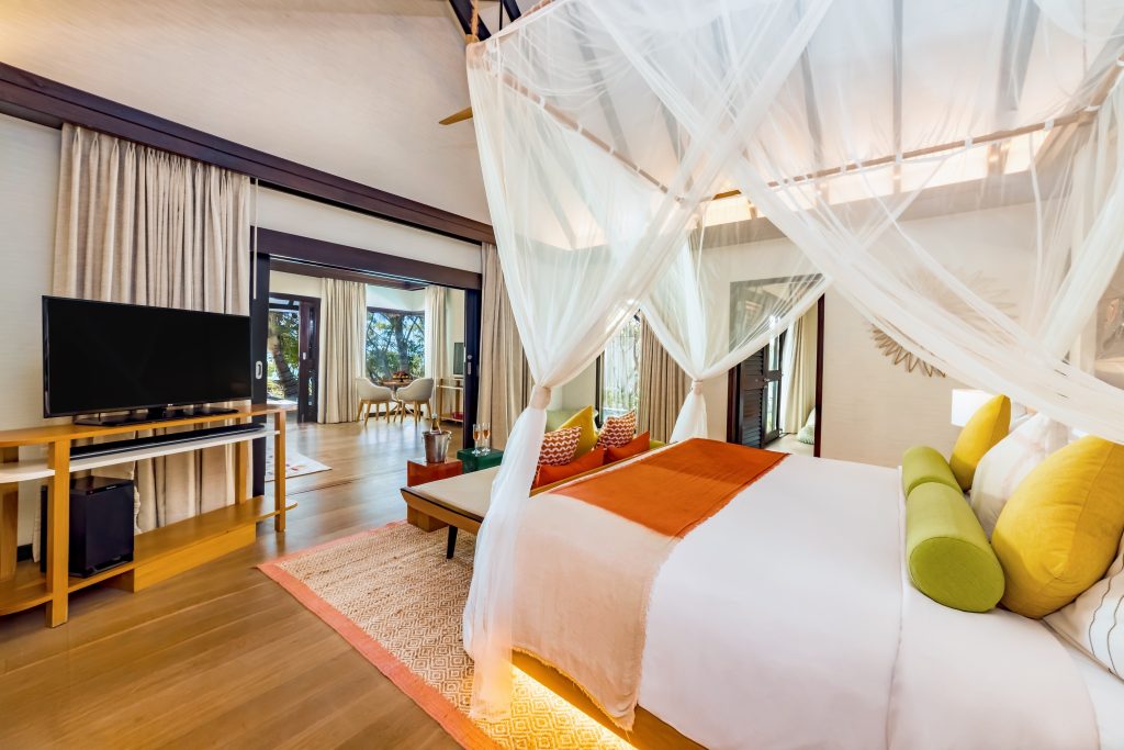 Hell eingerichtetes Zimmer im Ozen Life Maadhoo Earth Pool Pavilion mit großem Bett, Moskitonetz und Fernsehgerät