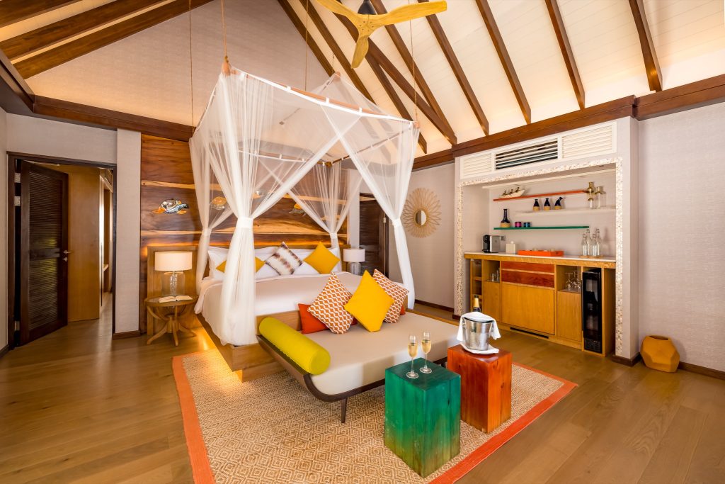 Helles Zimmer der Earth Villa im Ozen Life Maadhoo mit Himmelbett, Holzpaneelen, Teppich und warmem Licht