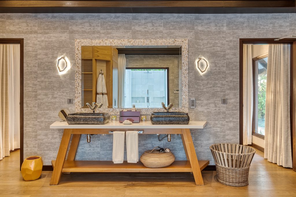 Badezimmer der Earth Villa mit zwei dunklen Steinschalenbecken auf Holzablage im Ozen Life Maadhoo Malediven
