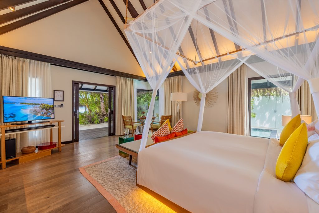 Zimmer der Earth Villa mit Himmelbett, Holzfußboden, Sitzbereich, Fernseher und Terrasse mit Blick ins Grüne