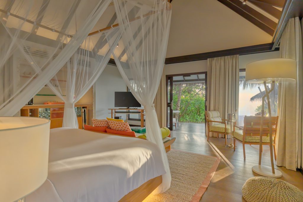 Zimmer der Earth Villa im Ozen Life Maadhoo mit Moskitonetz, Holzmöbeln, Terrasse und grüner Außenanlage auf den